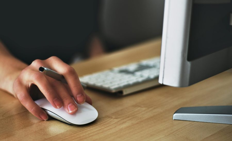 Free A hand using a wireless mouse at a modern desk setup with a computer and keyboard. Stock Photo